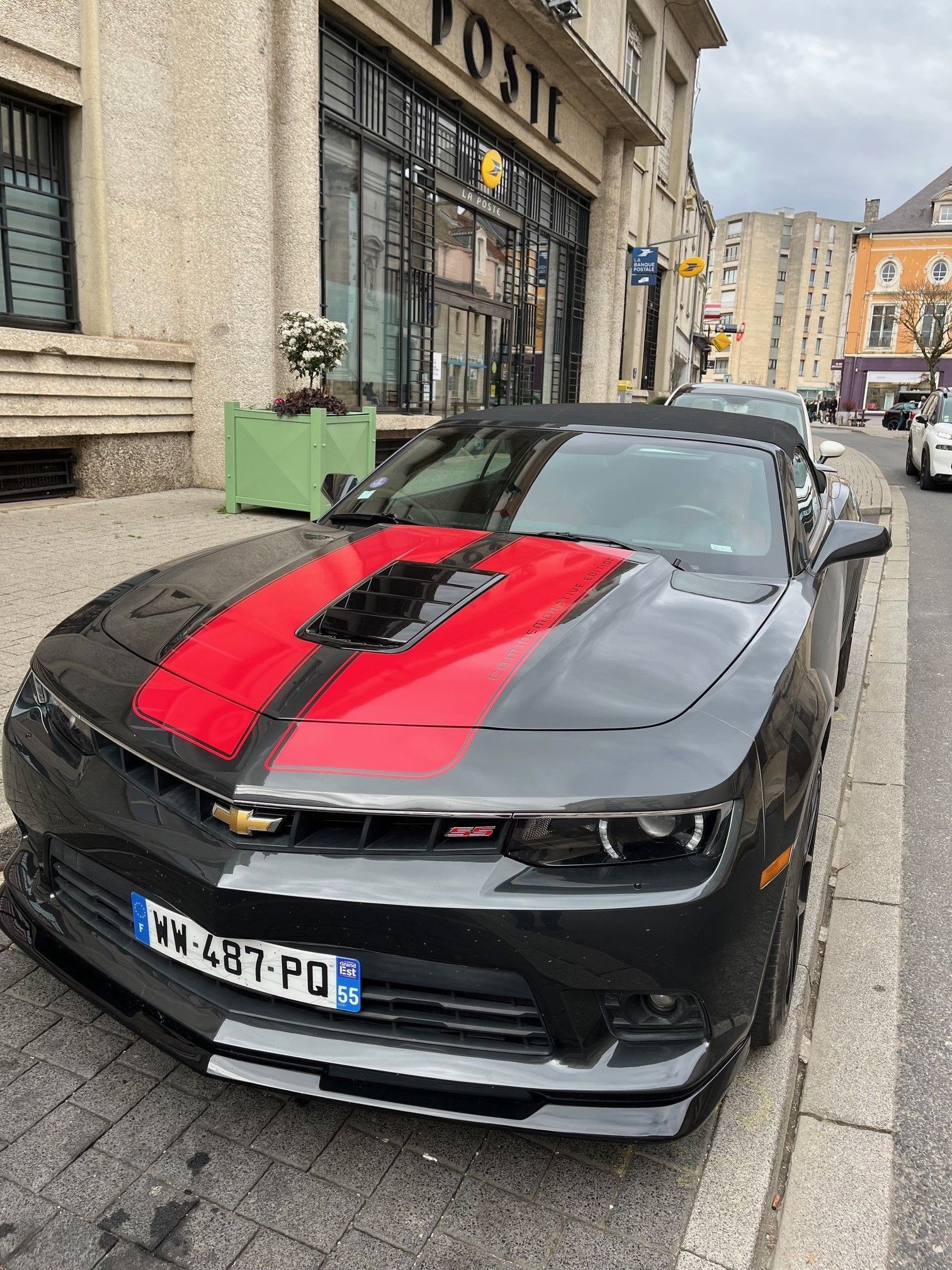 Une Chevrolet Camaro décapotable noire avec des bandes de course rouges est garée dans une rue de la ville.