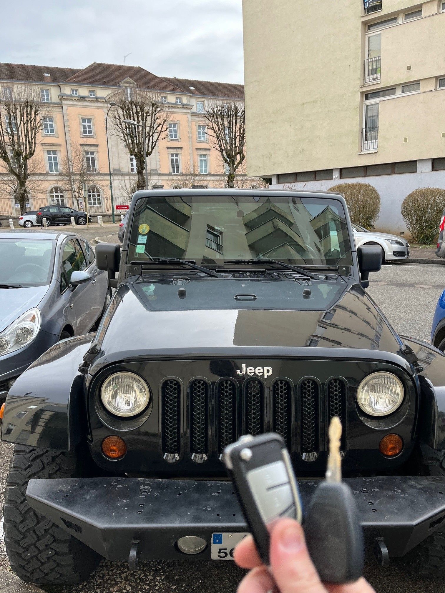 Jeep Wrangler noire, clés en main, garée devant des bâtiments par temps nuageux.