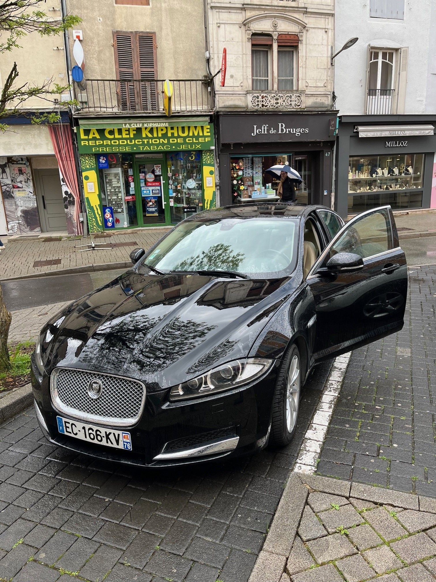 Jaguar noire garée dans une rue de la ville, portière ouverte. Immeubles en arrière-plan.