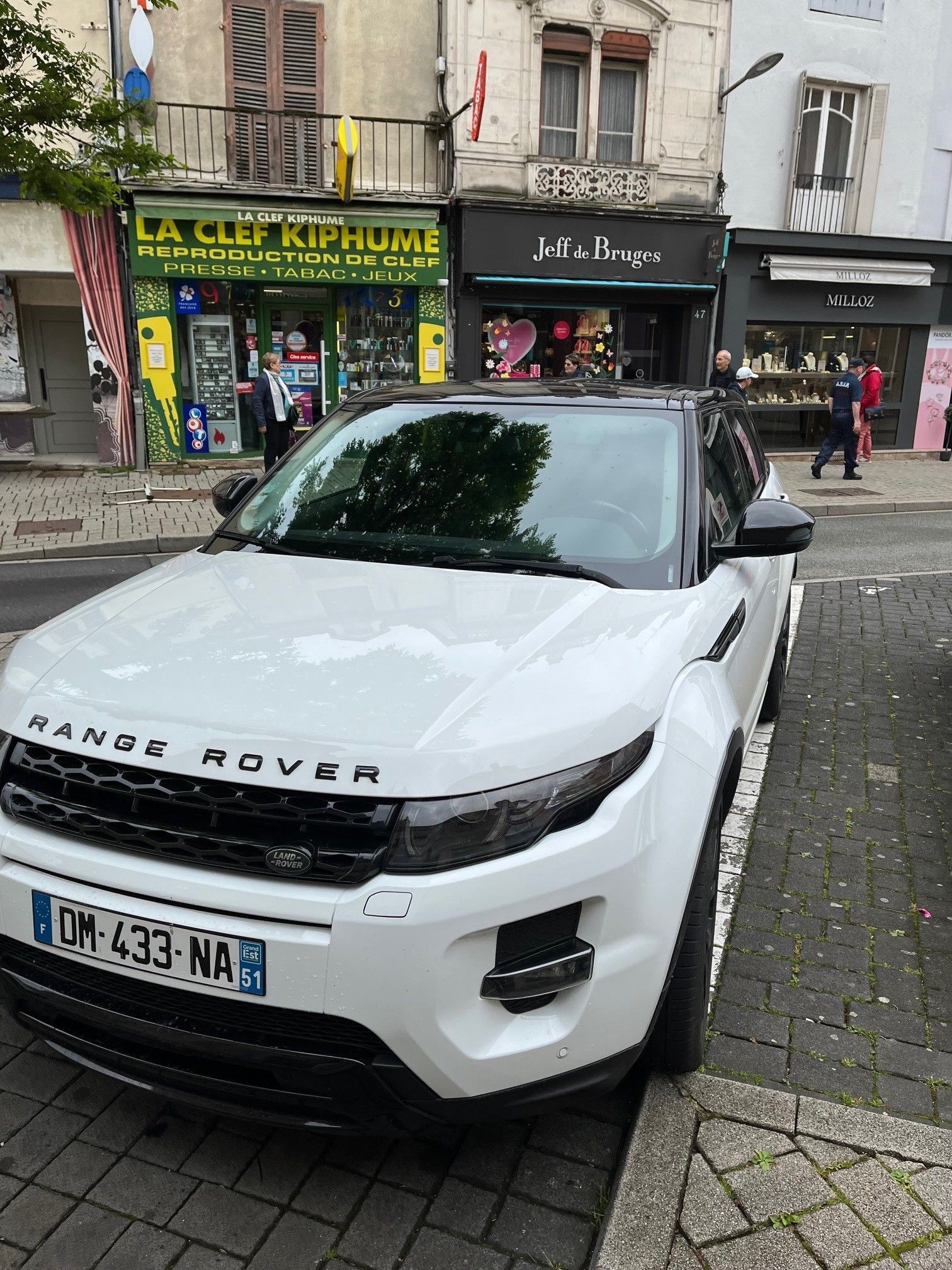 Un Range Rover blanc est garé dans une rue de la ville, devant des magasins.