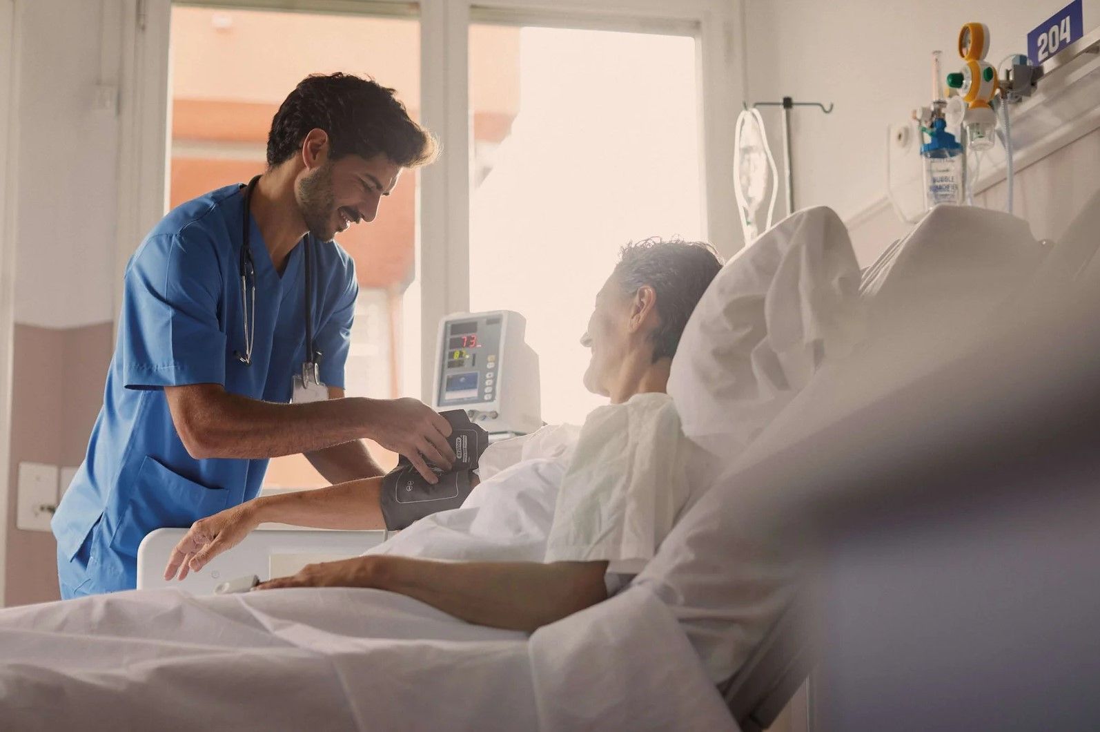 Un enfermero con uniforme azul toma la presión arterial de un paciente anciano en una cama de hospital.