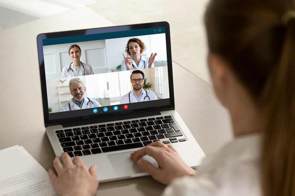 Una persona en una videollamada con cuatro médicos en una laptop. Los médicos conversan y gesticulan.