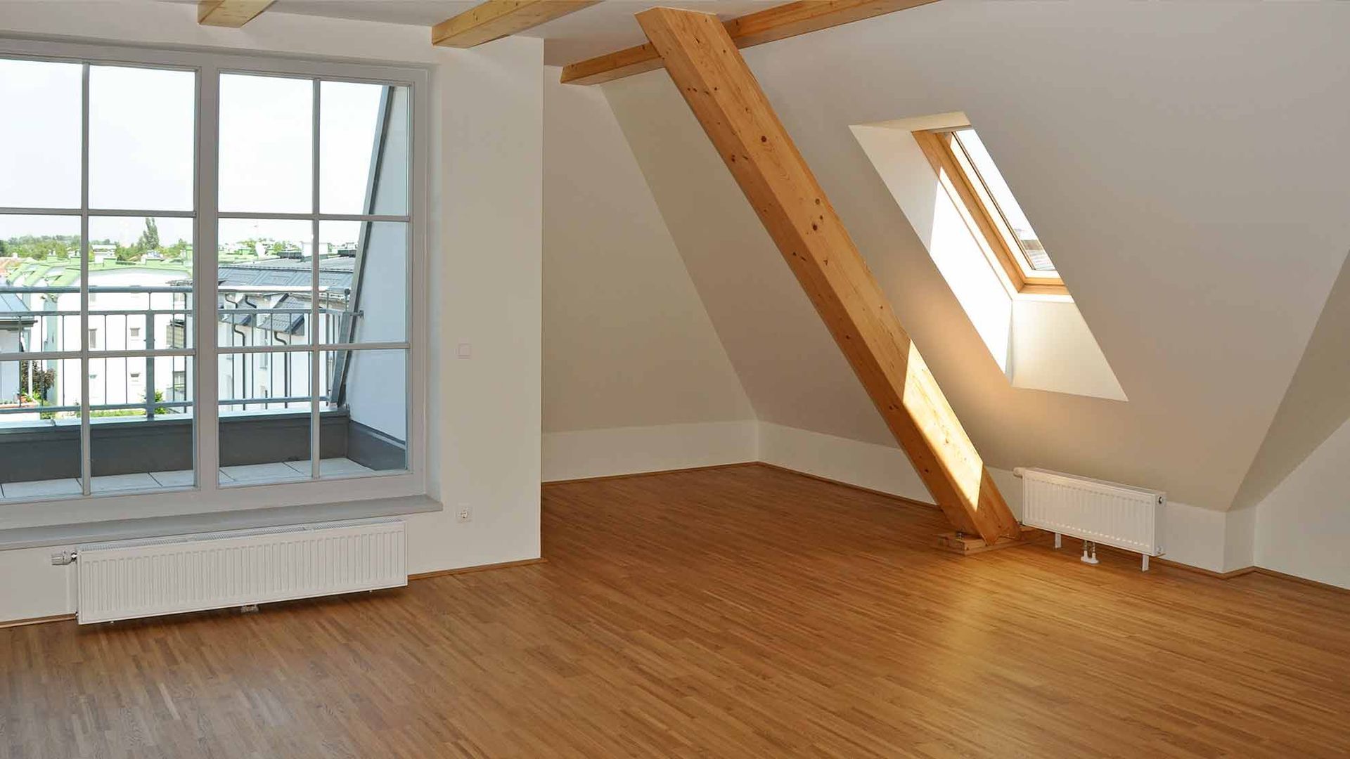 Leeres Dachzimmer mit Holzboden, Dachschräge, Dachfenster und großem Fenster mit Blick auf einen Balkon