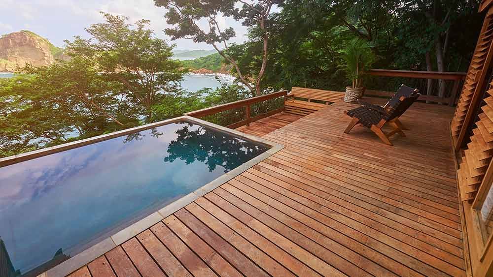 Eine Holzterrasse mit einem Swimmingpool und Stühlen darauf.