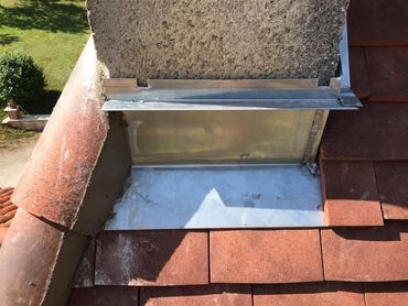 Gouttière et descente pluviale sur un toit de maison en tuiles rouges.