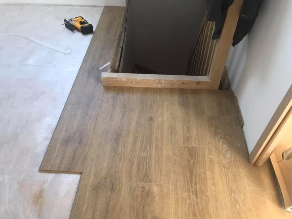 Une personne installe un parquet en étalant de la colle et en tapotant une lame pour la mettre en place.