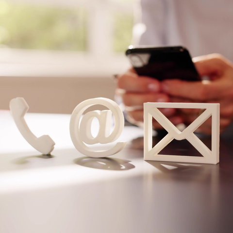 Des symboles de communication sont disposés sur une table, avec une personne utilisant un smartphone en arrière-plan.