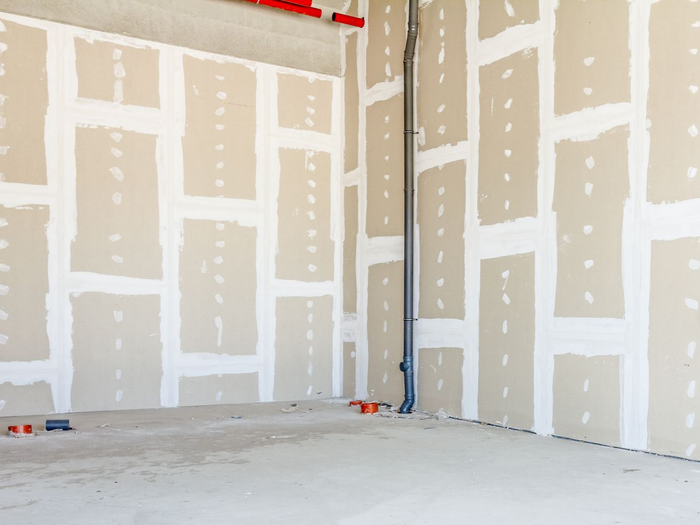 Pièce vide et inachevée avec cloisons sèches, joints apparents et sol en béton brut.