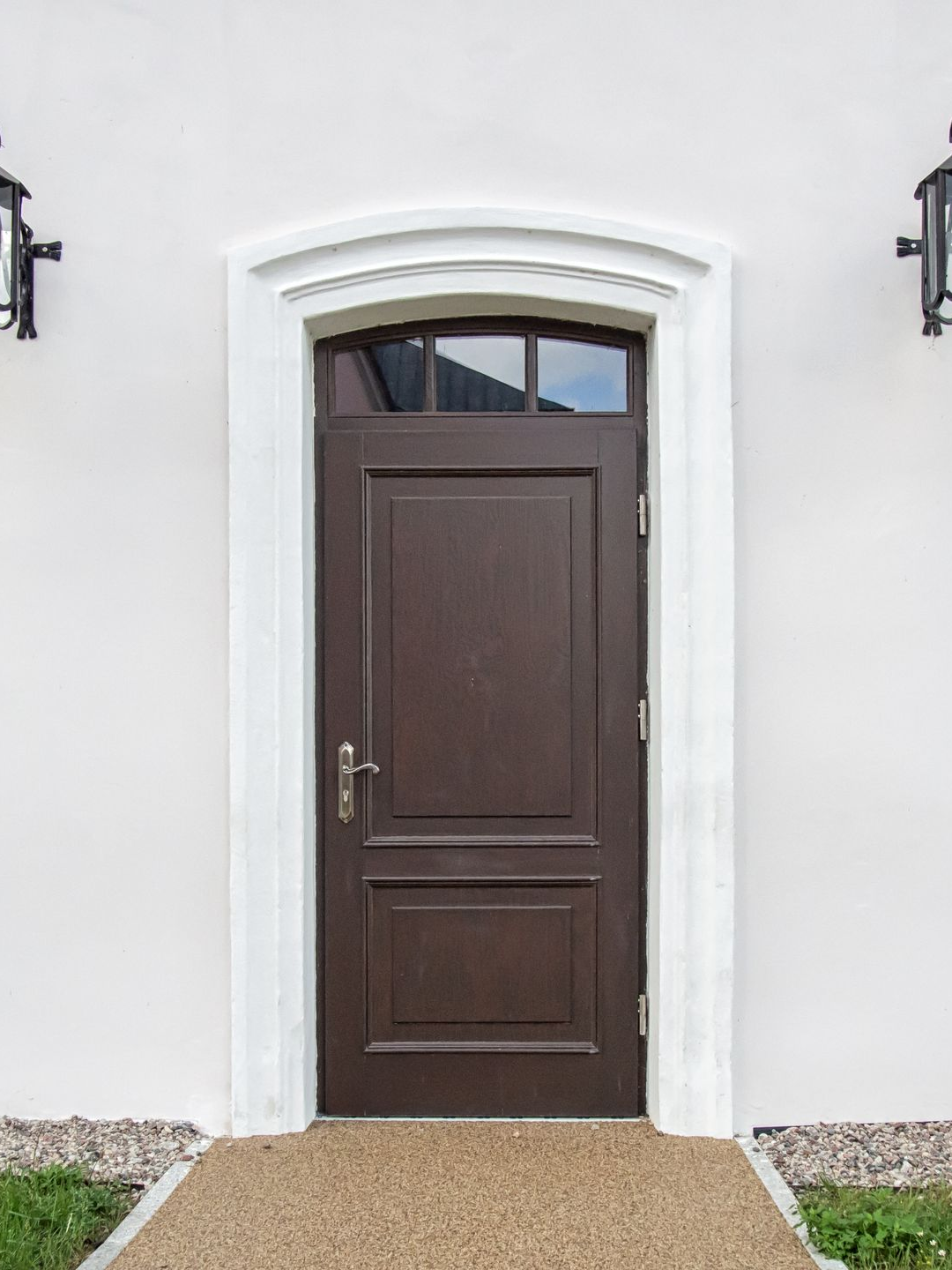Porte d'entrée vitrée en bois, encadrée par deux appliques murales.