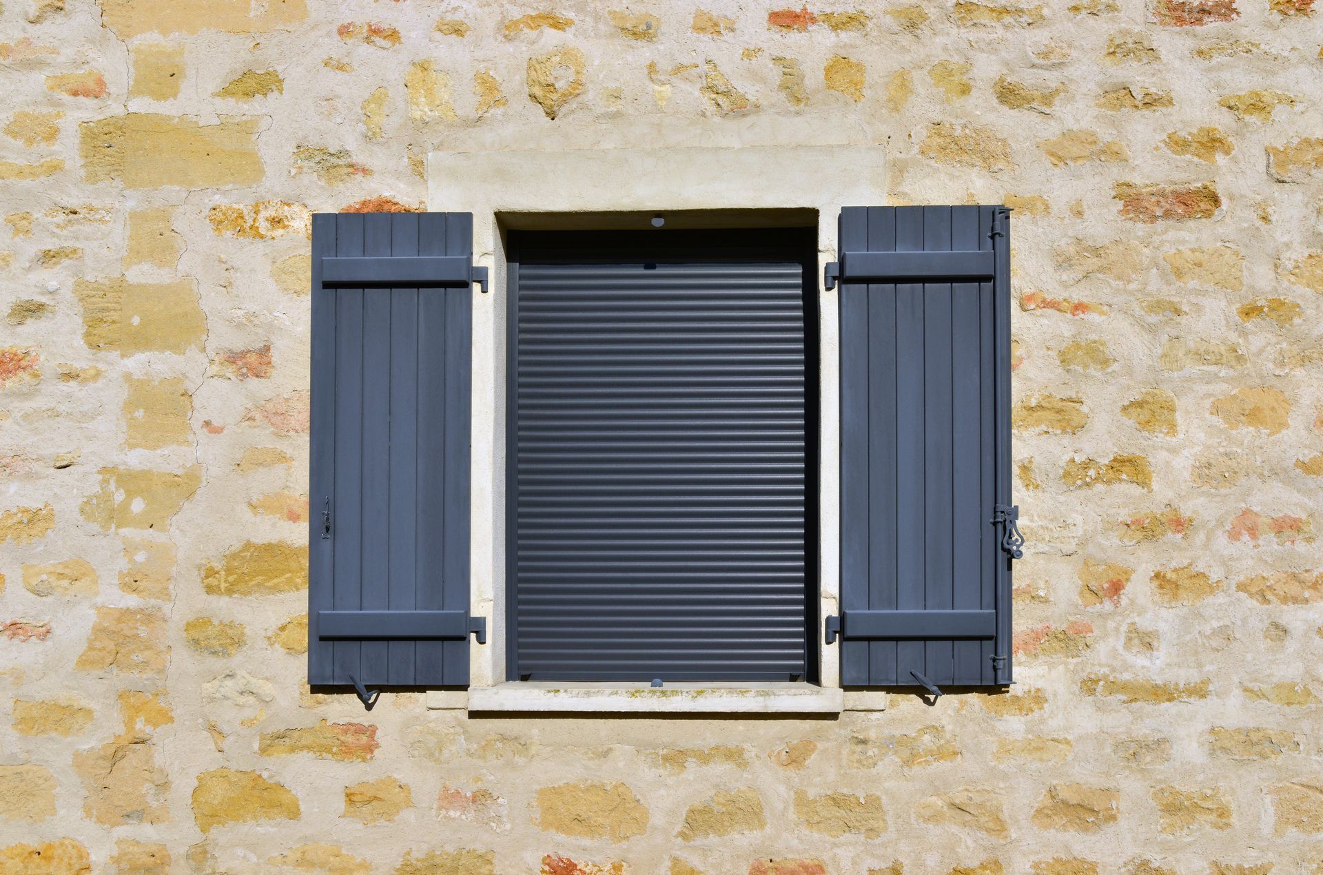 Mur en pierre avec une fenêtre centrale et des volets bleu foncé.