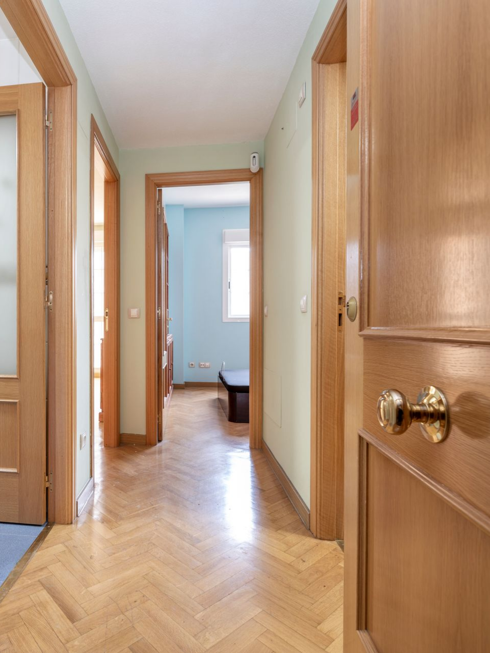 Couloir étroit avec portes en bois, parquet à chevrons.