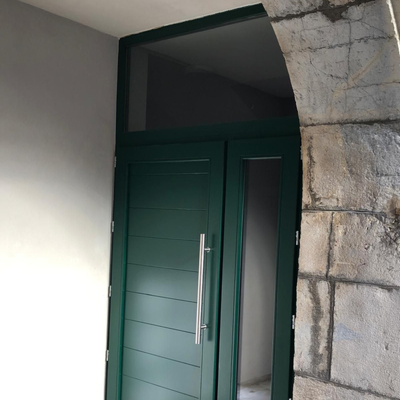 Porte d'entrée verte avec panneau de verre, dans une alcôve en pierre.