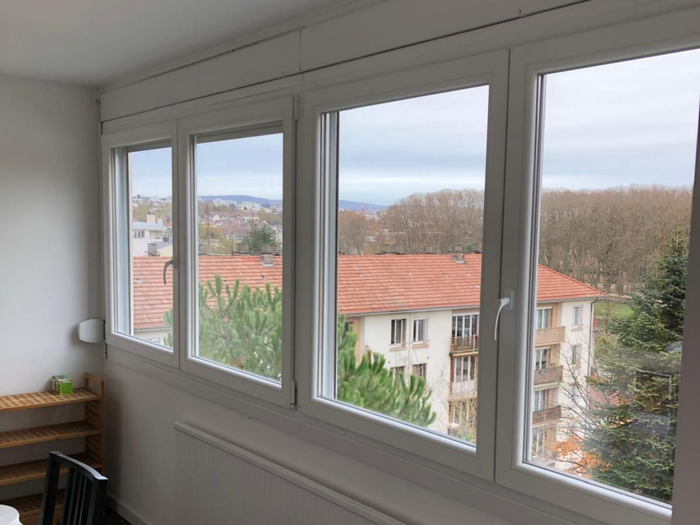 Fenêtres d'appartement lumineuses donnant sur des immeubles aux toits rouges et des arbres.