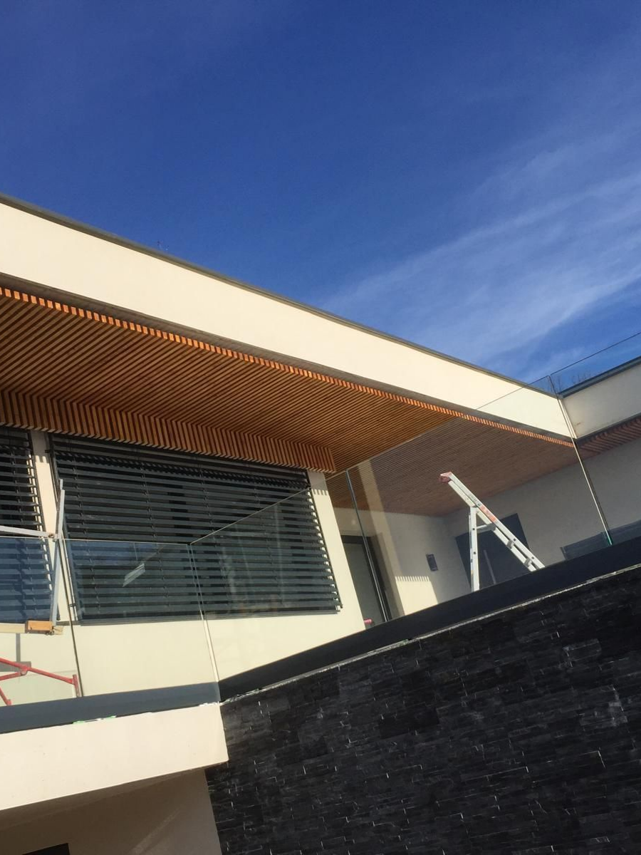 Vue en contre-plongée d’une maison contemporaine avec terrasse en verre, structure beige et finitions bois.