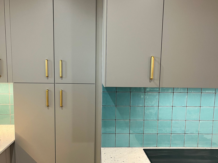 Cuisine moderne avec placards gris, poignées dorées, crédence en carrelage turquoise.
