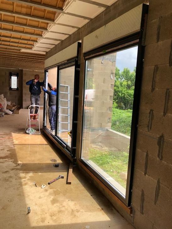 Deux ouvriers installent de grandes portes vitrées à cadre noir dans une maison en travaux.