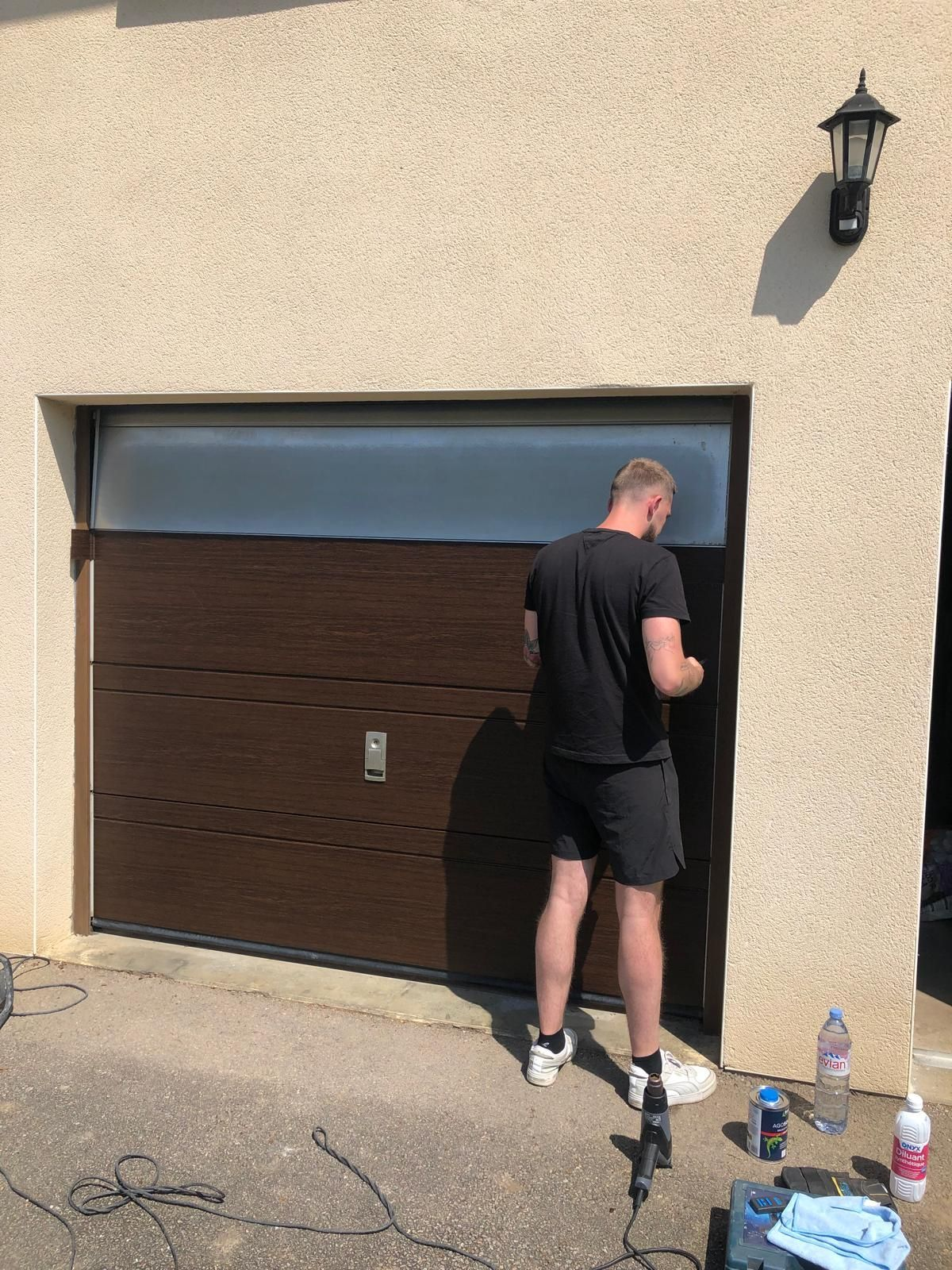 Une personne décape et peint une porte de garage en bois.