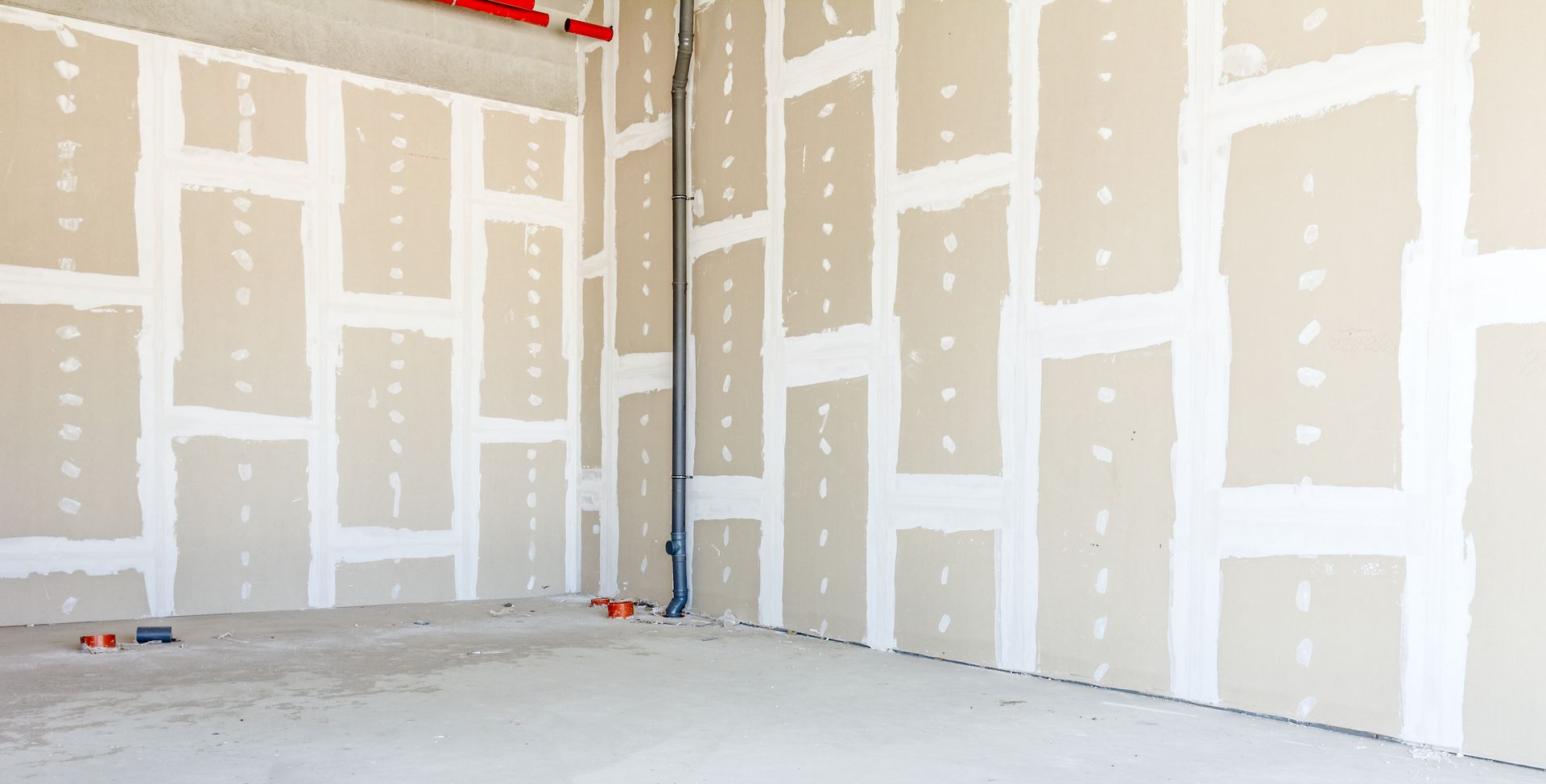 Pièce vide et inachevée avec des cloisons sèches beiges, des joints blancs et un sol en béton brut.