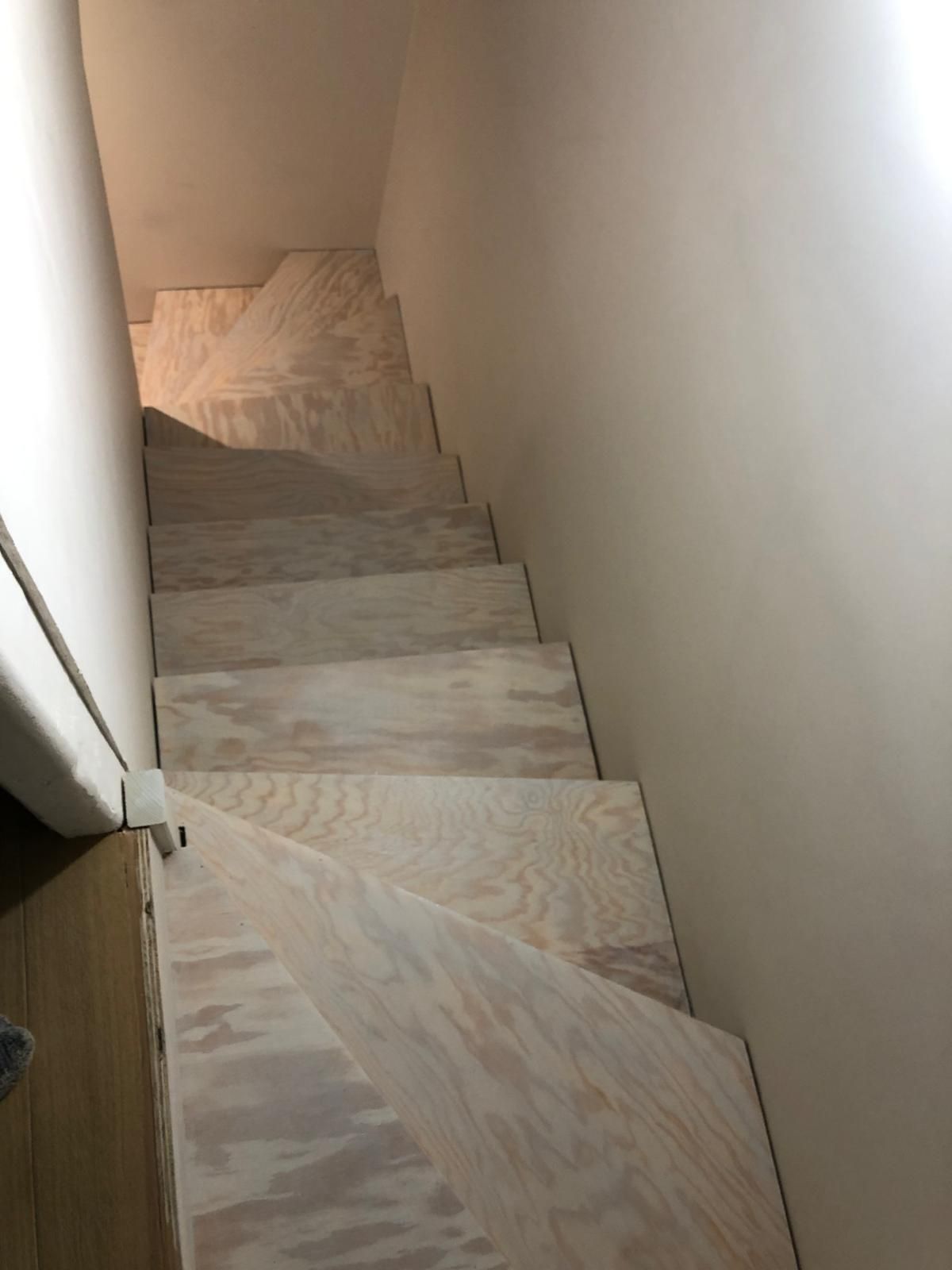 Escalier intérieur étroit aux marches claires et aux murs blancs, vu du haut.