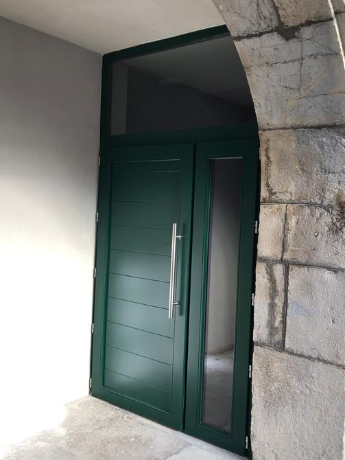 Porte en métal vert encastrée dans une arche en pierre à une entrée extérieure.