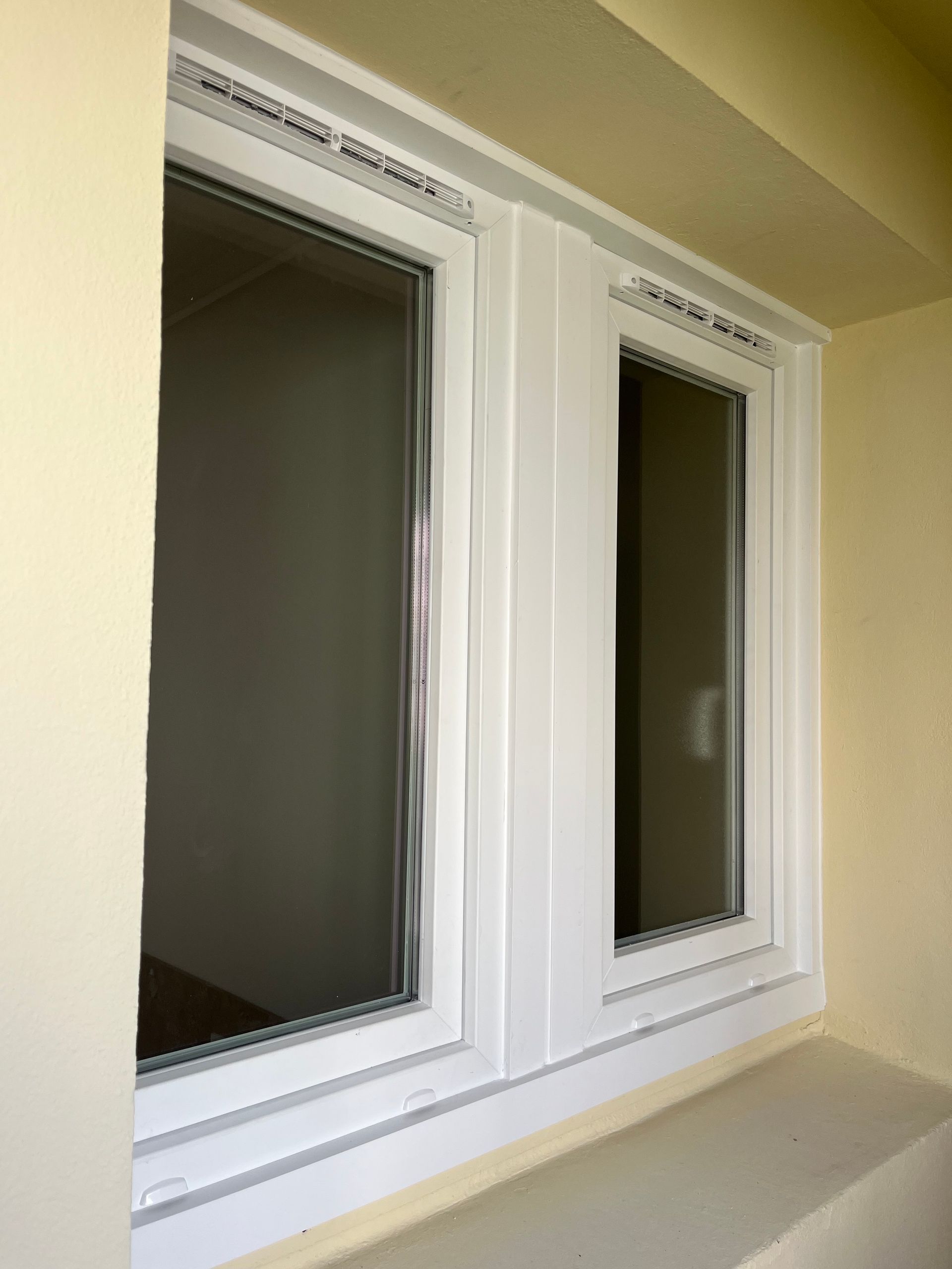 Deux fenêtres verticales à cadre blanc encastrées dans un mur beige avec un appui profond.