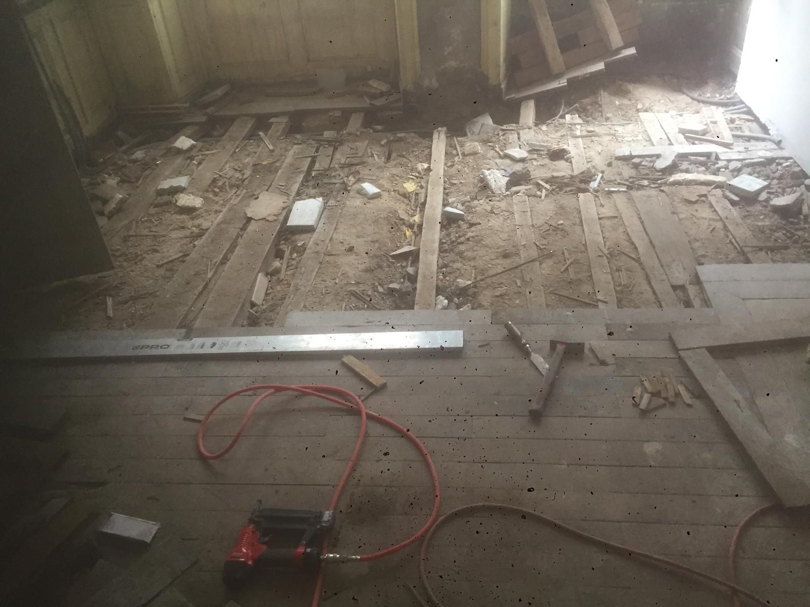 Chantier de rénovation avec plancher apparent, outils éparpillés et rallonge électrique rouge.