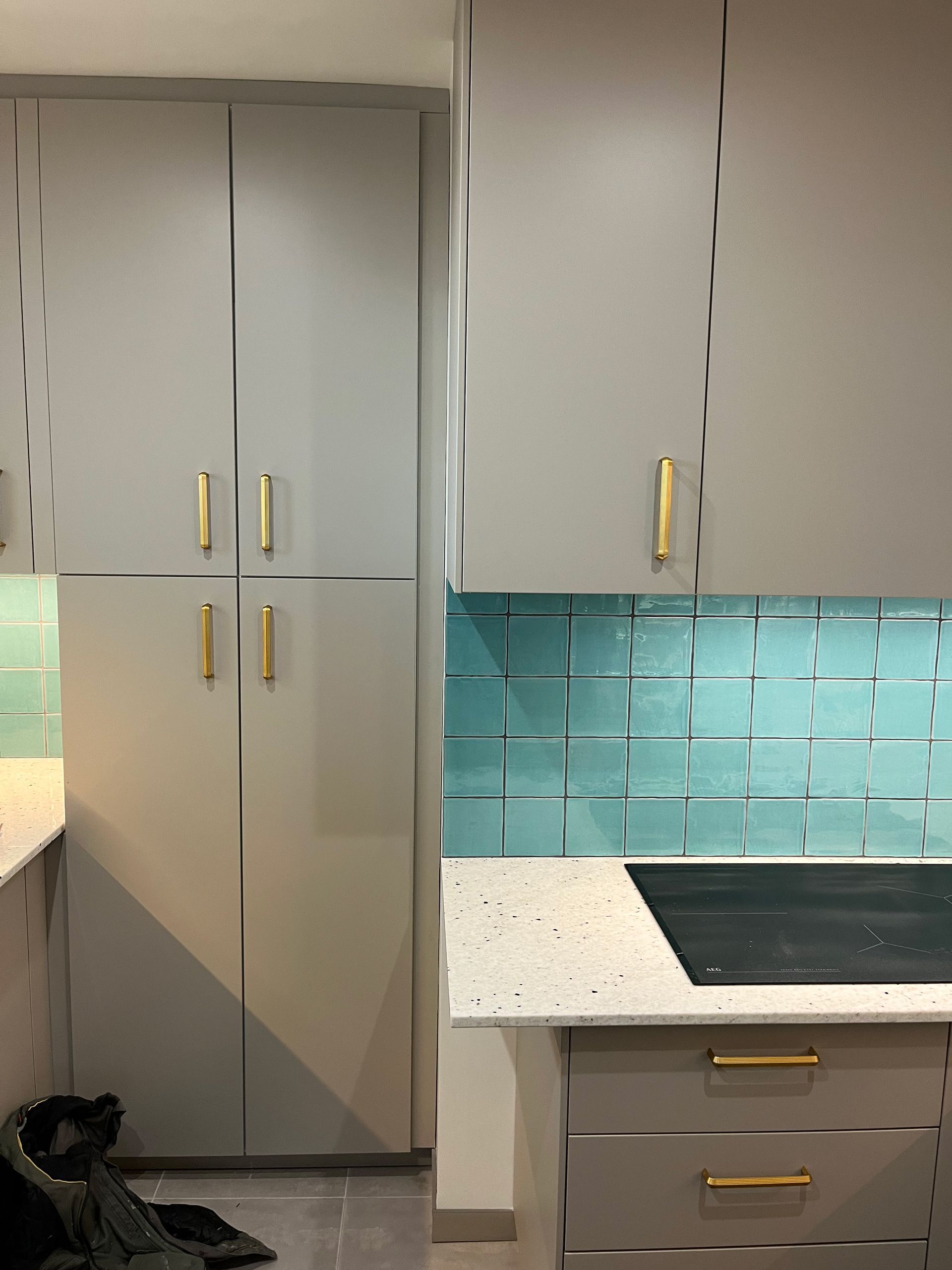 Cuisine moderne avec armoires grises, poignées dorées, crédence en carrelage turquoise et plaques induction.