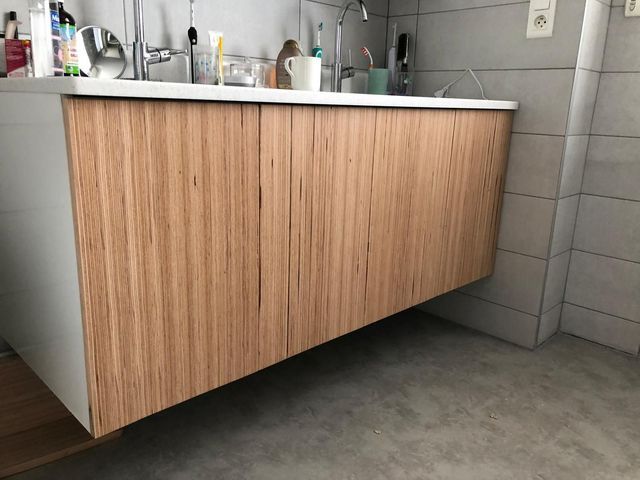 Meuble lavabo en bois avec deux vasques blanches, des murs carrelés et des produits de beauté.