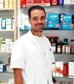 Un hombre con una bata blanca está de pie frente a un estante en una farmacia.