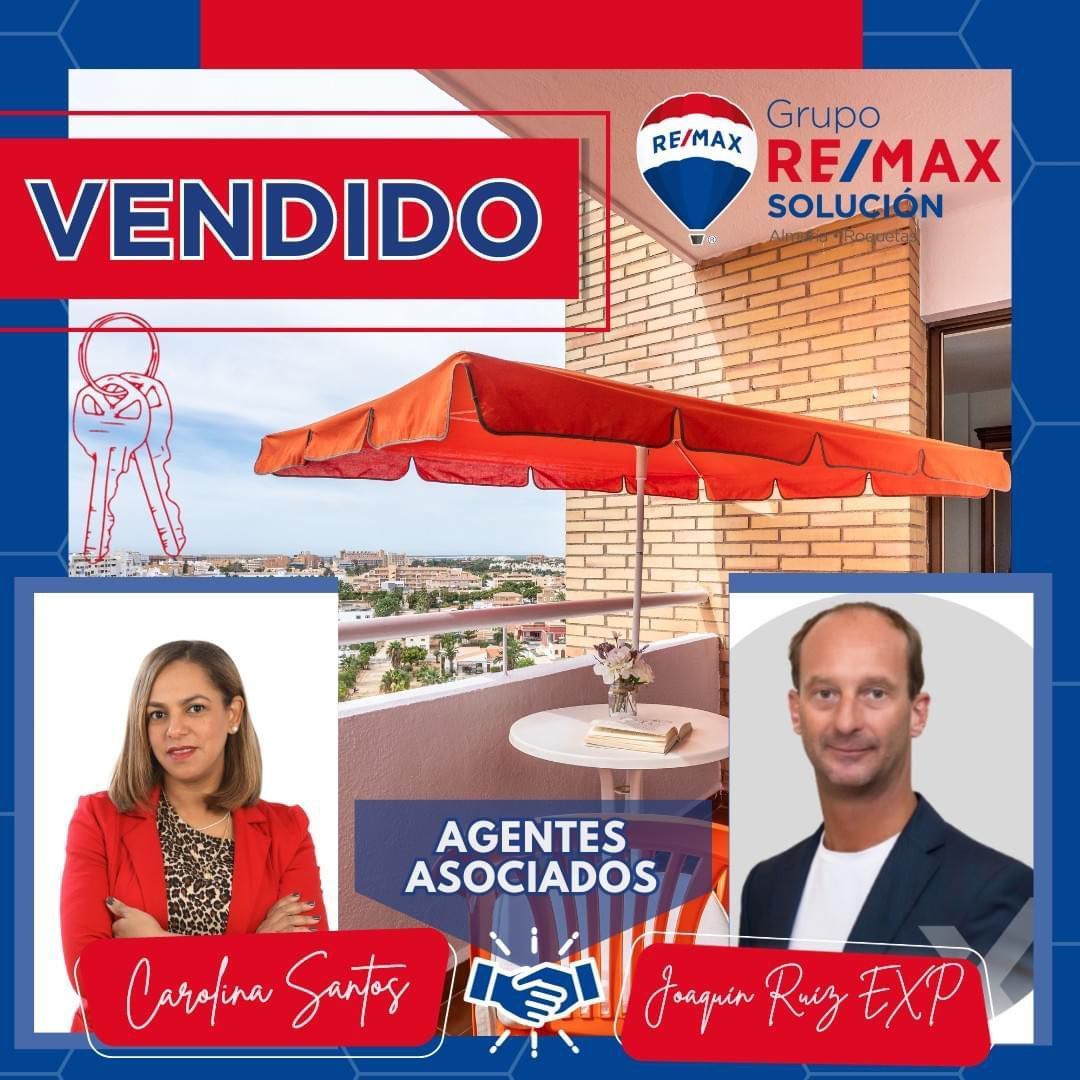 Un hombre y una mujer se dan la mano frente a un cartel de RE/MAX.