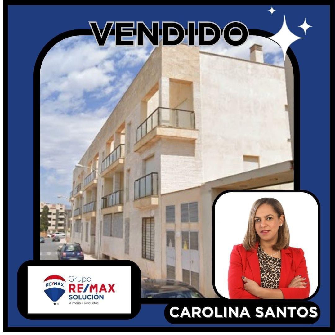 Una mujer con una chaqueta roja está parada frente a un edificio que dice vendido