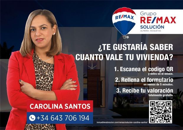 Una mujer con una chaqueta roja está parada frente a un cartel de RE/MAX.