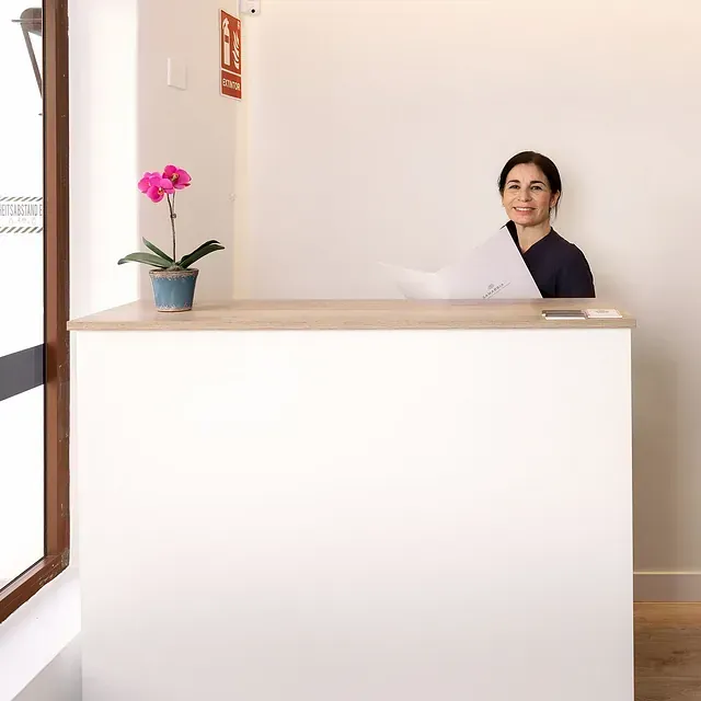 Una mujer está sentada en un mostrador de recepción con una flor rosa en una maceta.