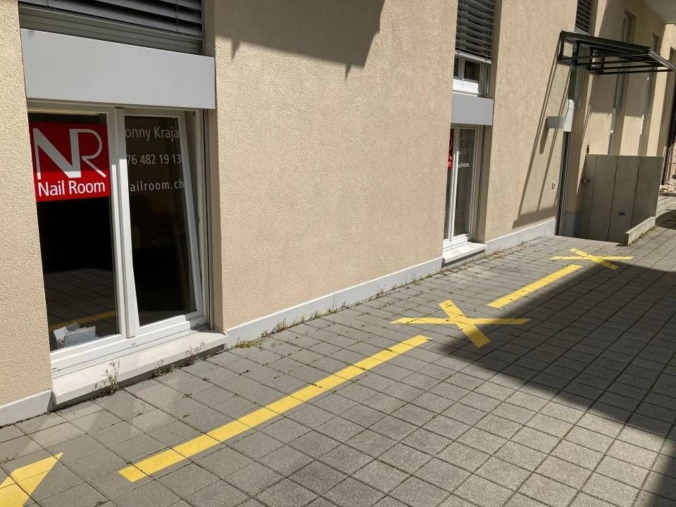 Gelbe Pfeile auf dem Bürgersteig weisen den Verkehr zu einem Nagelstudio mit einem Schaufensterschild.