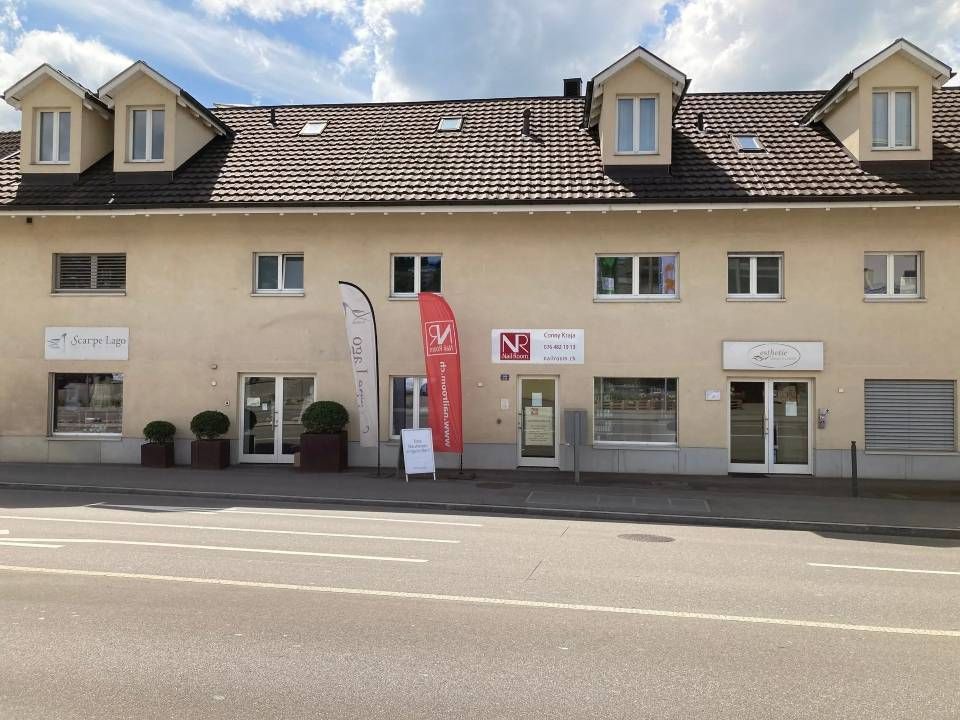 Beiges Geschäftsgebäude mit Läden und Dachgauben, Bürgersteig, Straße, klarer Himmel.