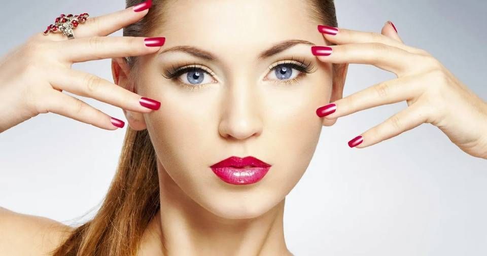 Frau mit rotem Lippenstift und Nagellack, die ihr Gesicht berührt, mit blauen Augen und einem Pferdeschwanz.