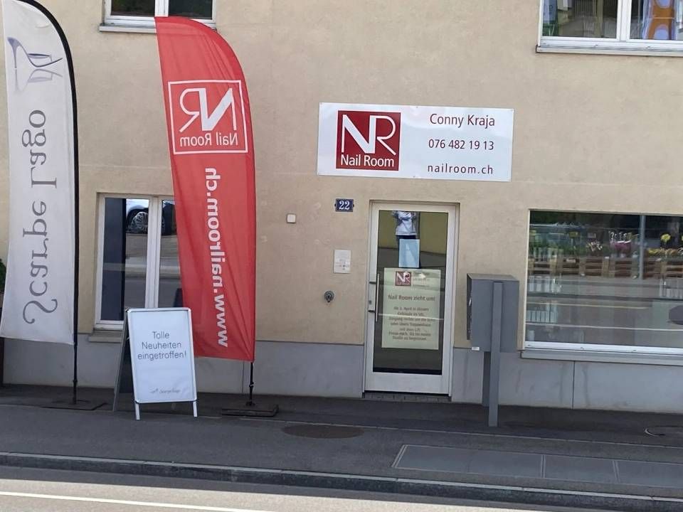 Außenansicht von Nail Reinery, einem Geschäft mit einem rot-weißen Schild, Fahnen und einem A-förmigen Schild.