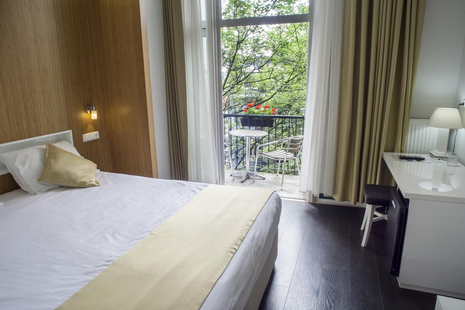 Hotel room with a made bed, desk, lamp, and balcony view through sliding glass doors
