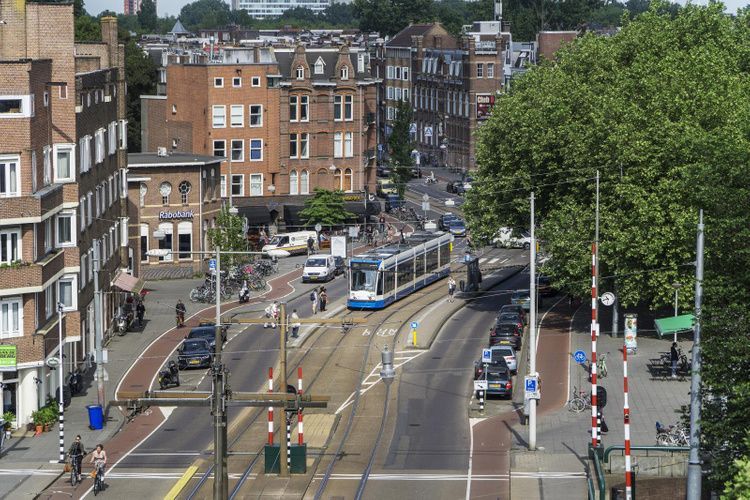 Tram on a city street with cars, tracks, brick buildings, and trees on a sunny day