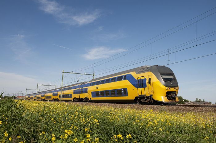 Yellow passenger train on tracks in a grassy field under a blue sky