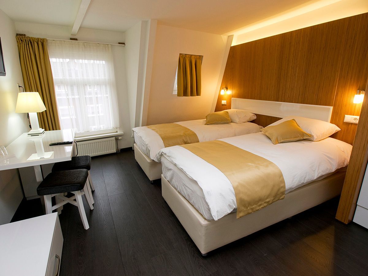 Hotel room with twin beds, wooden headboard, desk by the window, and warm bedside lamps