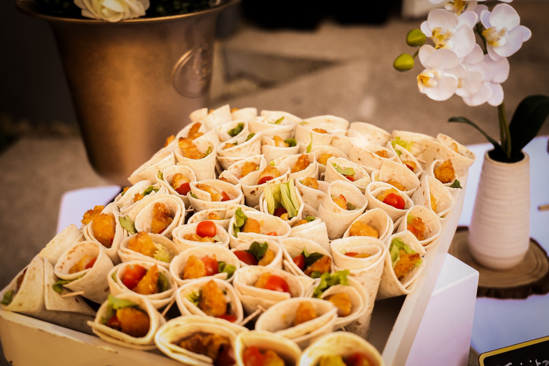Plateau de petits rouleaux de printemps garnis de légumes sur un buffet, avec des fleurs à côté.