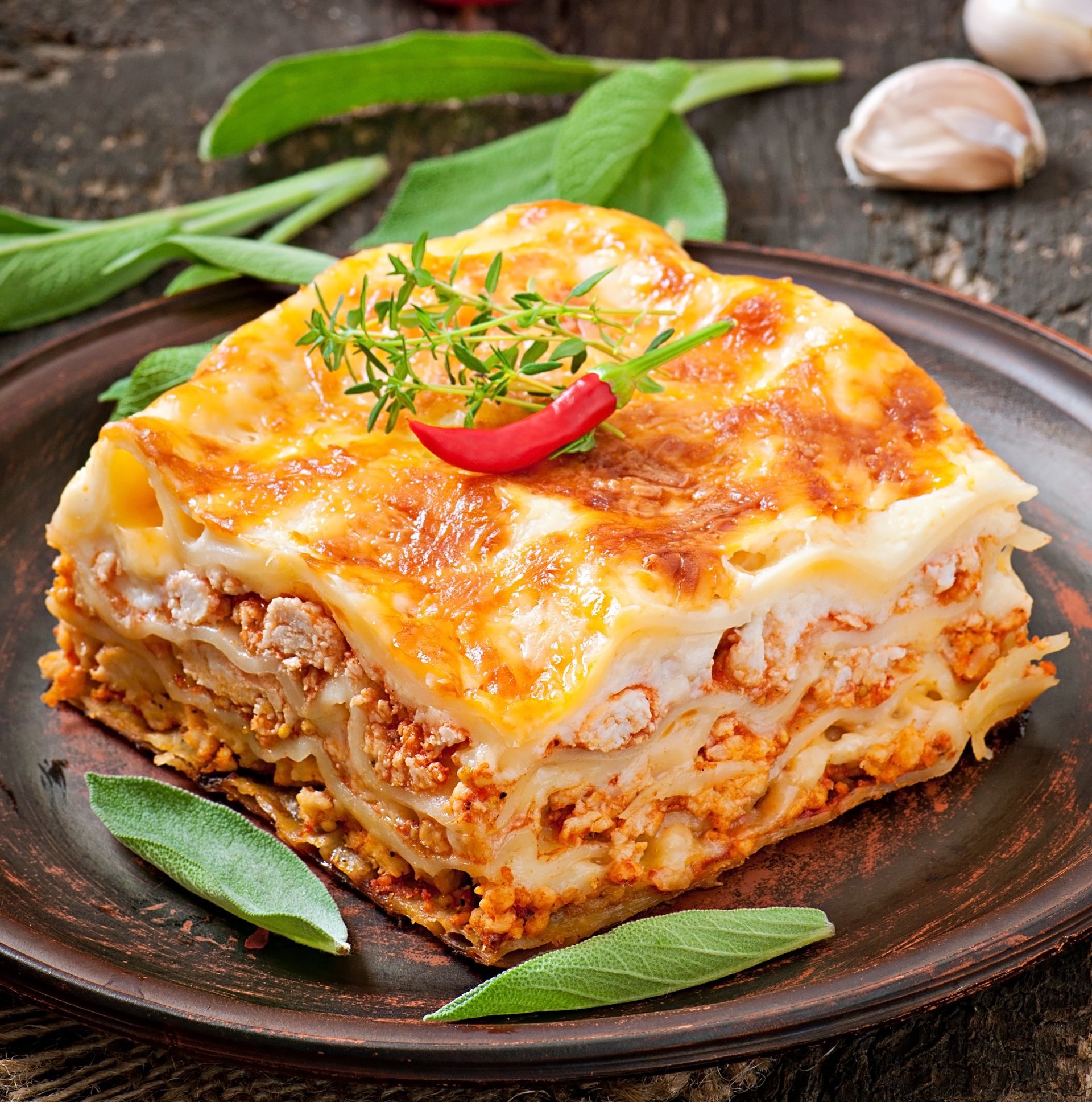 Une part de lasagnes cuites au four, garnie de fromage fondu et d'herbes aromatiques, servie dans une assiette.