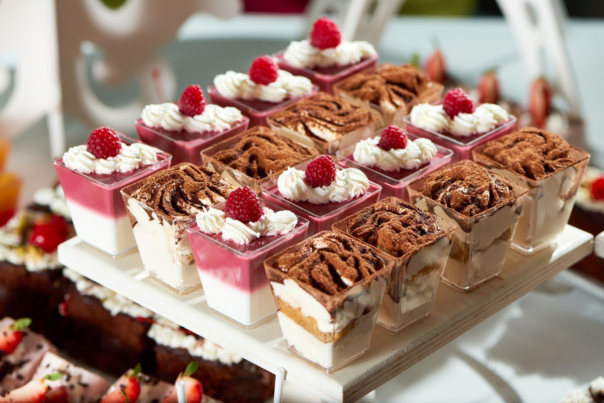 Assortiment de verrines à étages garnies de crème, de chocolat et de framboises, présentées sur un plateau blanc