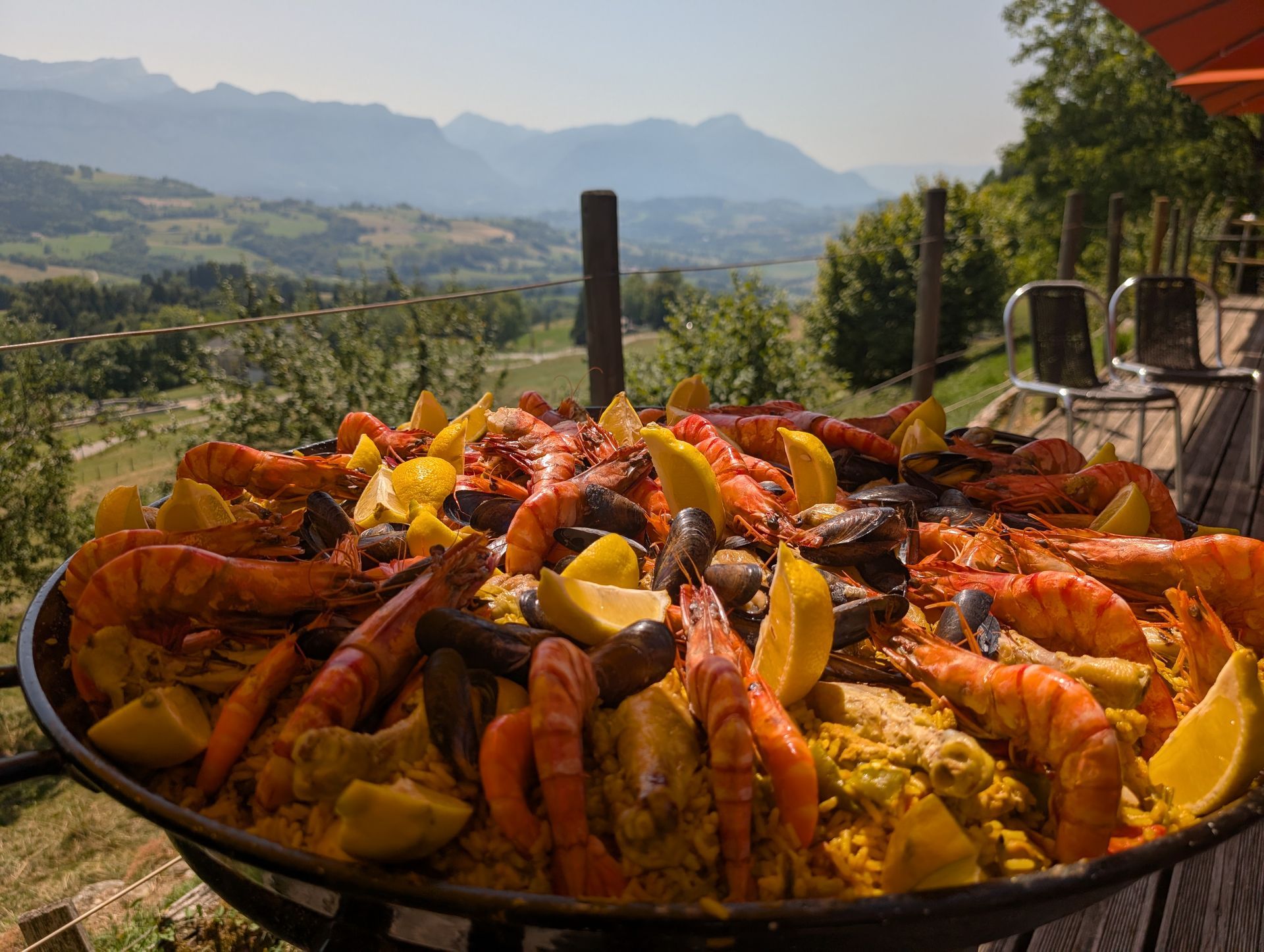Grande poêle de paella aux fruits de mer et aux citrons, servie en extérieur avec vue sur une vallée de montagne.
