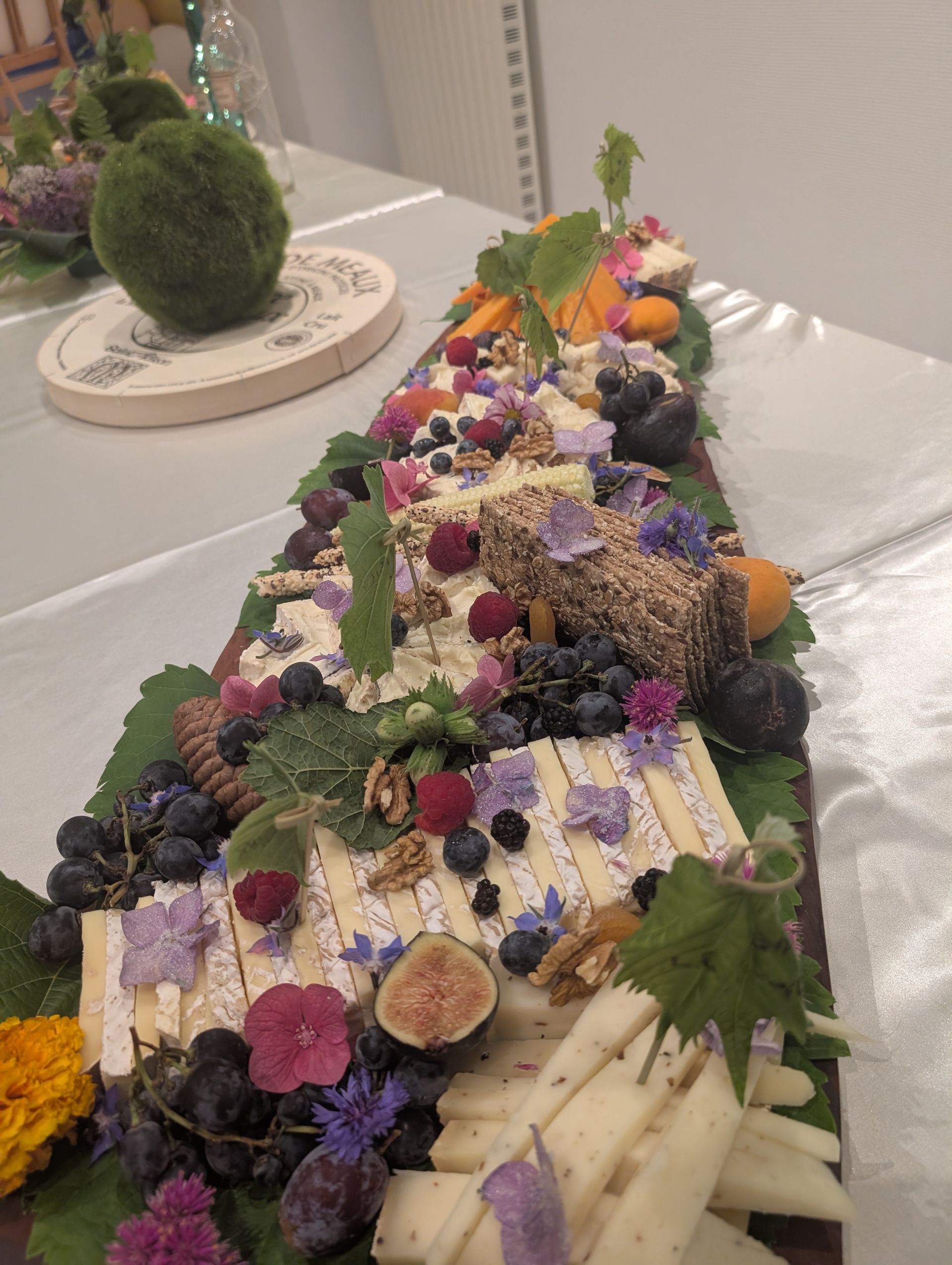 Composition florale colorée sur une longue table avec des fleurs violettes, blanches, oranges et vertes