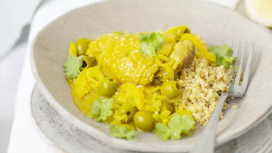 Poulet et légumes en sauce jaune servis dans un bol blanc avec du riz, sur une nappe légère, accompagnés d'une fourchette.