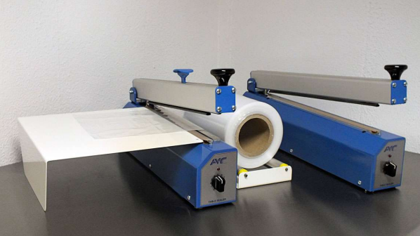 Blau-graue Industriemaschine mit einer weißen Materialrolle auf einer schwarzen Tischplatte