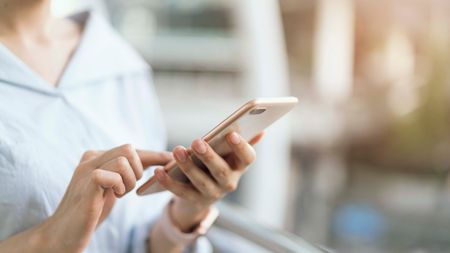Eine Person benutzt in einem Innenraum ein Smartphone und tippt mit beiden Händen auf den Bildschirm.