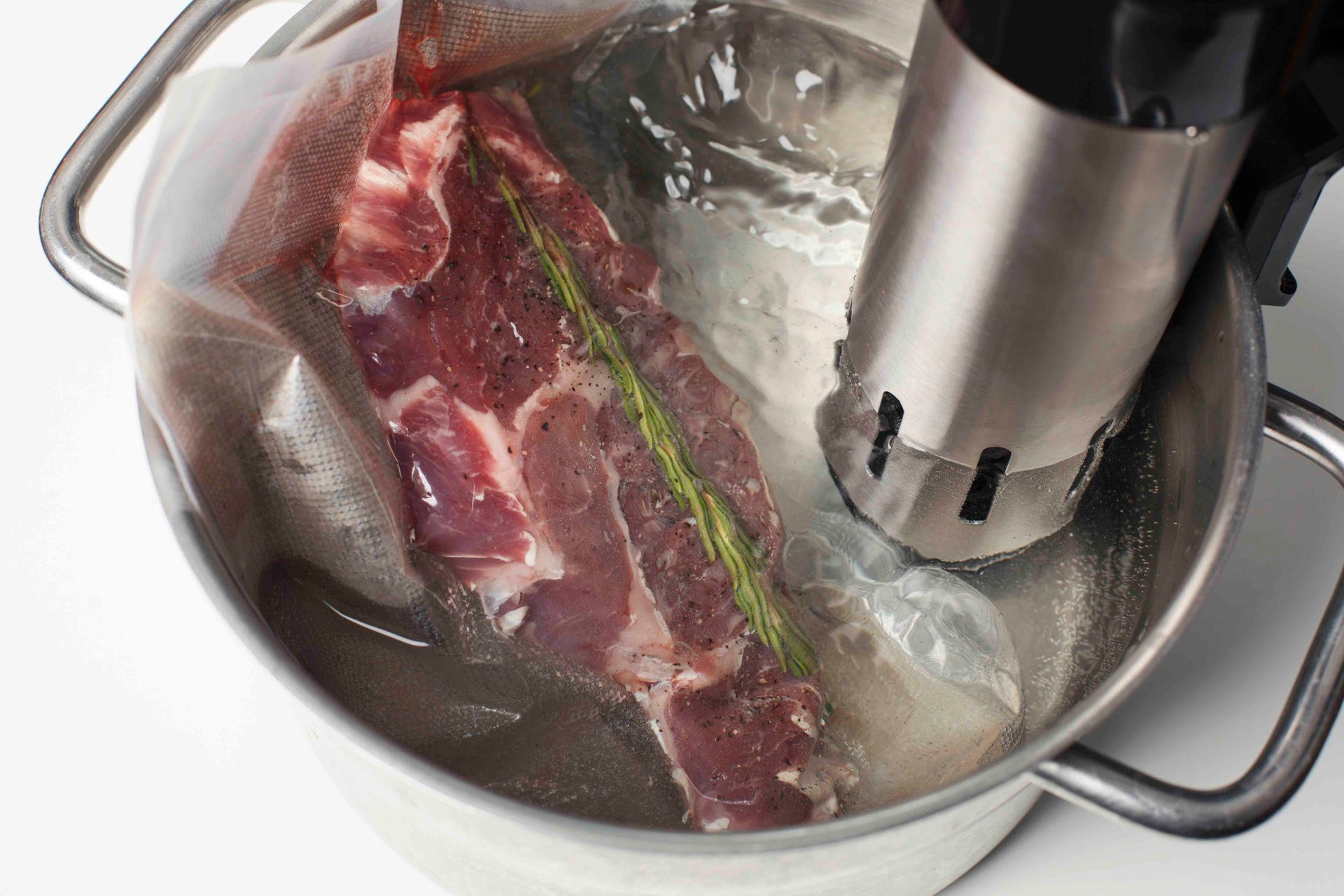 Vakuumverpacktes rohes Fleisch in einem Topf mit Wasser, das mit einem Sous-vide-Gerät gegart wird.